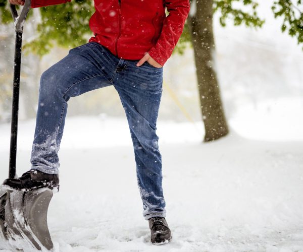 A closeup shot fo a male with his foot on the snow shovel while standing in a snowy field