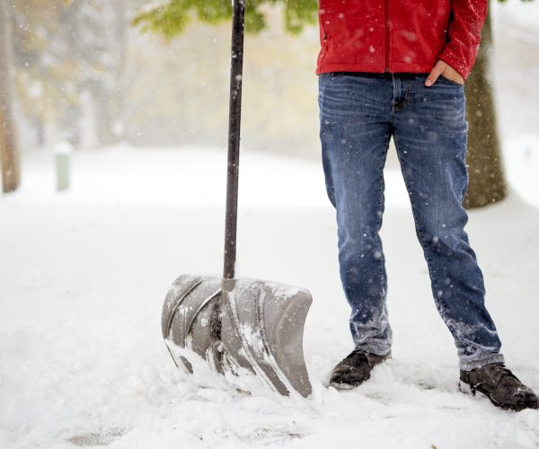 A male standing on a snowy field and holding a snow shovel with a blurred background